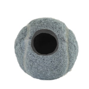 May include: A gray tennis ball with a large, circular opening. The ball has a fuzzy texture and a dark interior. The opening is lined with a black material. The ball is designed for pet use.