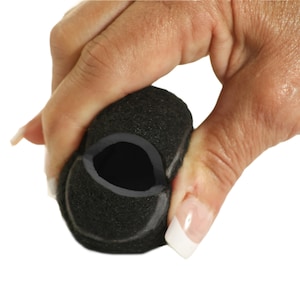 May include: A black foam microphone cover is held in a hand against a white background. The cover has a dark gray interior and is made of a porous material. The hand is holding the cover, partially compressing it.
