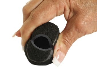 May include: A black foam microphone cover is held in a hand against a white background. The cover has a dark gray interior and is made of a porous material. The hand is holding the cover, partially compressing it.