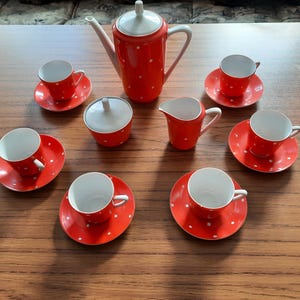 Könnte beinhalten: Ein rotes Vintage-Teeservice mit weißen Punkten, bestehend aus einer Teekanne, einem Milchgießer, einer Zuckerdose und sechs Tassen mit Untertassen. Das Set steht auf einem Holztisch.