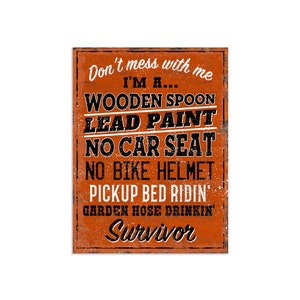 May include: Orange and black distressed sign with the text "Don't mess with me I'M A... WOODEN SPOON LEAD PAINT NO CAR SEAT NO BIKE HELMET PICKUP BED RIDIN' GARDEN HOSE DRINKIN' Survivor"
