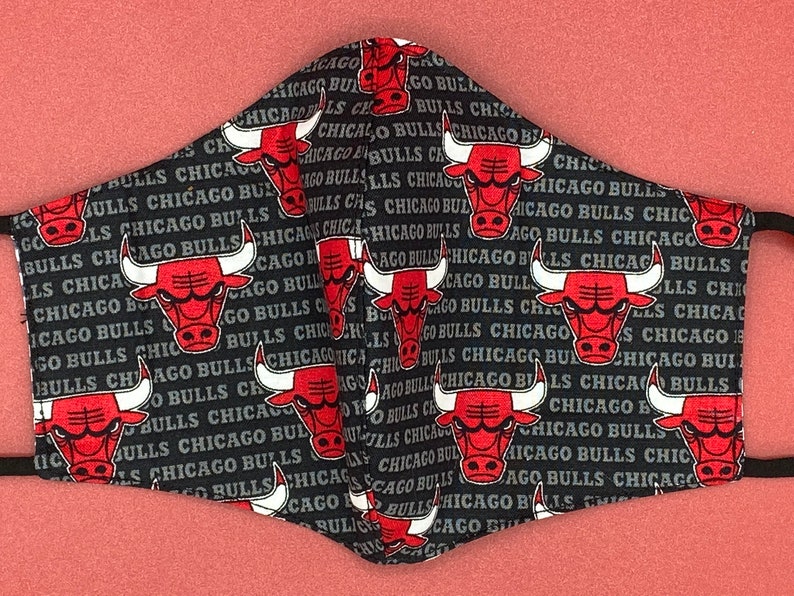May include: Black face mask with a repeating pattern of red Chicago Bulls logos and the words "Chicago Bulls" in white.