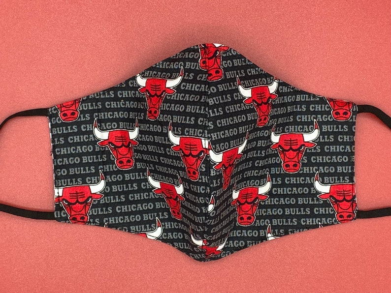 May include: Black face mask with a repeating pattern of red Chicago Bulls logos and the text "Chicago Bulls" in white.