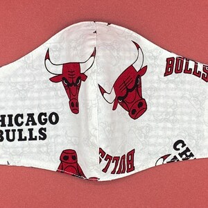 Puede incluir: M&aacute;scara facial blanca con un patr&oacute;n repetido de logotipos rojos de los Chicago Bulls y el texto "Chicago Bulls" y "Bulls".
