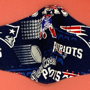 Puede incluir: Una mascarilla facial azul con un patr&oacute;n repetido del logotipo de los New England Patriots, estrellas y las palabras "Patriots" y "New England".