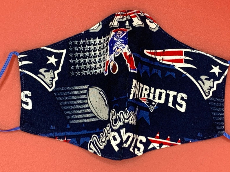 Puede incluir: Una mascarilla facial azul con un patr&oacute;n repetido del logotipo de los New England Patriots, estrellas y las palabras "Patriots" y "New England".