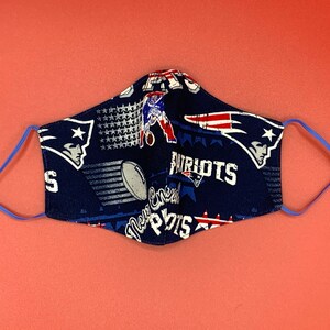 Puede incluir: Una mascarilla facial azul con un patr&oacute;n del logotipo de los New England Patriots, estrellas y las palabras "Patriots" y "New England".