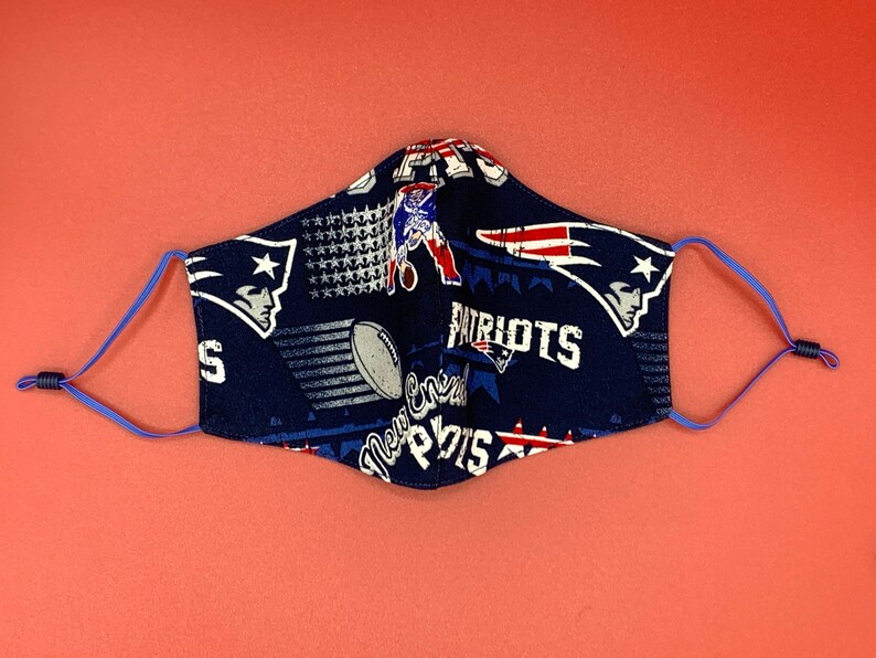 Puede incluir: Una mascarilla facial azul con un patr&oacute;n del logotipo de los New England Patriots, estrellas y las palabras "Patriots" y "New England".