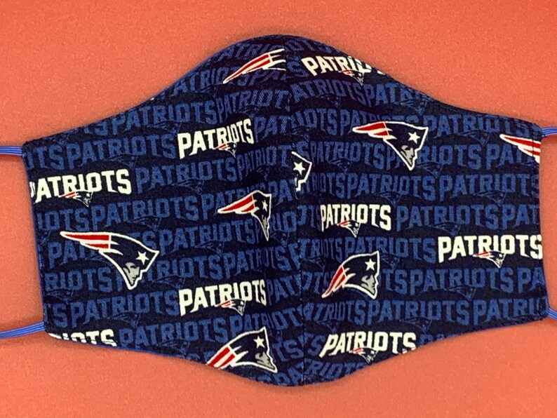 Puede incluir: Una mascarilla facial azul con un patr&oacute;n repetido del logotipo de los New England Patriots y la palabra "Patriots" en blanco.