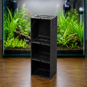Puede incluir: Una carcasa de filtro de acuario negra, rectangular y de tres niveles hecha de plástico. La estructura cuenta con compartimentos frontales abiertos con estantes ranurados y ranuras de ventilación laterales, diseñados para colocación vertical.