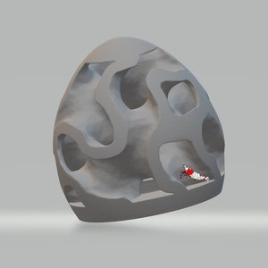 Puede incluir: Una estructura gris, de forma de cueva, impresa en 3D, con un peque&ntilde;o camar&oacute;n rojo y blanco en su interior. La estructura tiene muchos agujeros y t&uacute;neles.