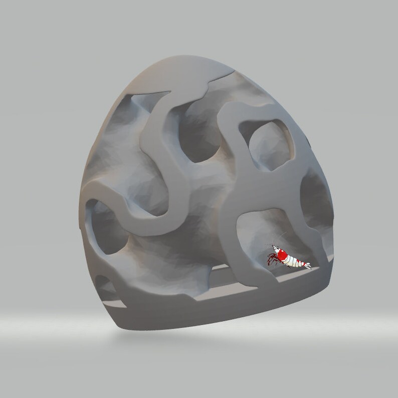 Puede incluir: Una estructura gris, de forma de cueva, impresa en 3D, con un peque&ntilde;o camar&oacute;n rojo y blanco en su interior. La estructura tiene muchos agujeros y t&uacute;neles.