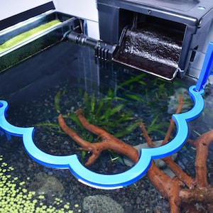 Puede incluir: Un acuario con un sistema de filtración y una herramienta azul en forma de onda. El tanque contiene agua, plantas y madera flotante. El filtro es negro y la herramienta está dentro del tanque.