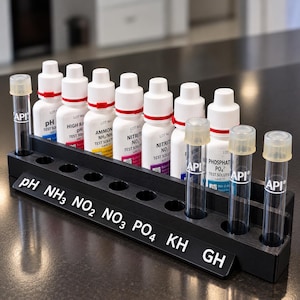 Può includere: Un supporto per test in plastica nera contenente diversi flaconi contagocce bianchi etichettati pH, High Range pH, Ammonia, Nitrite, Nitrate e Phosphate, insieme a tre provette in vetro trasparente con tappi e marchio API bianco.