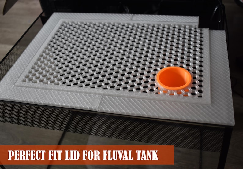 May include: A white, perforated lid for a Fluval tank with a diamond-patterned border. An orange, circular component sits on the lid. The text "PERFECT FIT LID FOR FLUVAL TANK" is displayed in a brown banner at the bottom.