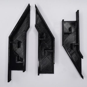 May include: Three black plastic pieces with intricate designs, possibly for a model or a craft project.