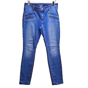 May include: Blue denim jeans with a faded wash. The jeans have multiple zipper pockets on the front and a button closure. The jeans are hanging on a metal hanger.