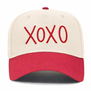May include: A baseball cap with a cream-colored crown and a red brim. The embroidered text "XOXO" in red is centered on the front. The cap has a red button on top.
