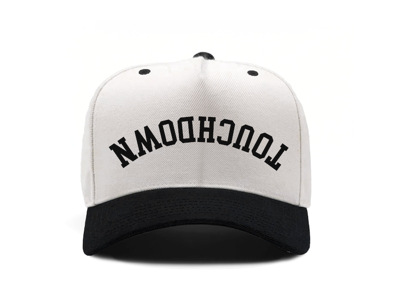 Puede incluir: Gorra de b&eacute;isbol blanca con visera negra. La parte delantera de la gorra tiene el texto "TOUCHDOWN" escrito en negro.
