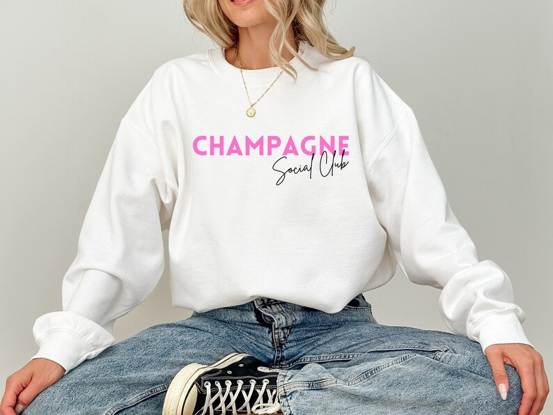 May include: White sweatshirt with the text "Champagne Social Club" in pink lettering.