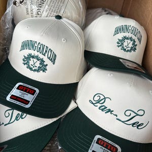 May include: Several white and green baseball caps are visible. The caps display the text "Hanning Golf Club" and "Par Tee" in green. Each cap has a green peak and a small green button on the crown.