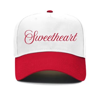 May include: A white baseball cap with a red brim and a red button on top. The word "Sweetheart" is written in red script across the front of the cap.