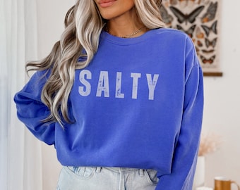 Könnte beinhalten: Ein blaues Sweatshirt mit langen Ärmeln und dem Aufdruck "SALTY" in Weiß auf der Vorderseite.