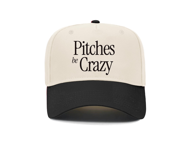 Op de afbeelding: Een beige en zwarte baseballpet met de tekst "Pitches be Crazy" in zwart.