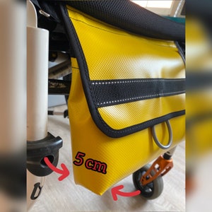 Może przedstawiać: Żółta wodoodporna torba z czarnym paskiem i srebrnym pierścieniem. Torba jest przymocowana do czarno-białego wózka. Torba ma 5 cm szerokości.