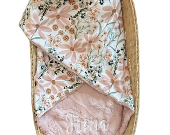 May include: A baby blanket with a floral pattern in a wicker basket. The blanket features a pink and white floral design on one side and a soft, pink, textured fabric with the name "Fiona" embroidered on the other side.