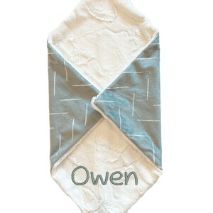 Puede incluir: Una manta suave para beb&eacute;, blanca y gris con un lazo de sat&eacute;n blanco. La manta tiene un patr&oacute;n geom&eacute;trico en un lado y una textura suave y peluda en el otro lado. La manta est&aacute; personalizada con el nombre "Owen".