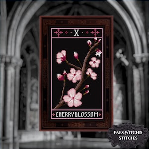 Puede incluir: Arte de punto de cruz de una rama de cerezo en flor con flores y capullos rosas sobre un fondo negro. La obra enmarcada incluye el texto "CHERRY BLOSSOM" y se presenta sobre un fondo oscuro de estilo gótico.
