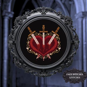May include: A framed cross-stitch design featuring a red heart pierced by three swords. The heart has dripping blood details. The black frame has ornate detailing. The text "FAES WITCHES STITCHES" is on a small plaque.
