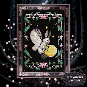 May include: A cross-stitch pattern on a black background featuring a white moth with brown antennae, positioned above a yellow circular object. The design is enclosed in a rectangular border of green leaves and pink flowers, framed in a dark ornate frame.