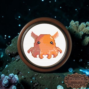 Puede incluir: Un punto de cruz enmarcado de un pulpo de dibujos animados en tonos naranja y rosa. La obra de arte está ambientada sobre un fondo oscuro con temática submarina con burbujas y coral. El marco es marrón y el texto "FAES WITCHES STITCHES" es visible.