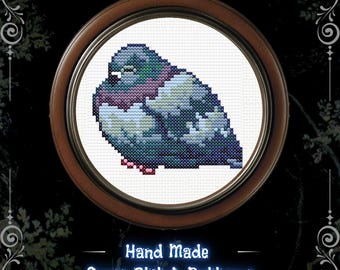 May include: A cross stitch pattern of a plump pigeon with blue, purple, and white plumage, enclosed in a circular wooden frame. Below the frame, the text reads Hand Made Cross Stitch Patterns FaesFortunes in a glowing blue font style.