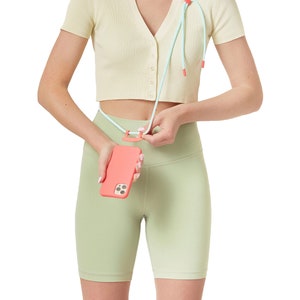 K&ouml;nnte beinhalten: Eine Person tr&auml;gt ein hellgelbes geripptes Crop-Top mit einem hellblauen und rosafarbenen Handyband. Das Band ist an einer rosa Handyh&uuml;lle befestigt. Die Person tr&auml;gt hellgr&uuml;ne Shorts.