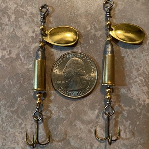 May include: Two gold fishing lures with bullet casings and treble hooks. The lures are about the size of a US quarter.