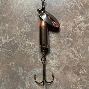 May include: A silver fishing lure with a bullet-shaped body and a silver blade. The lure has a triple hook.