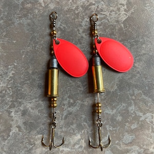May include: Two red and gold fishing lures with bullet-shaped weights and treble hooks.