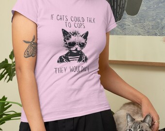 May include: A pink t-shirt with a black and white illustration of a cat wearing sunglasses and a jacket. The text on the shirt reads "If cats could talk to cops they wouldn't".