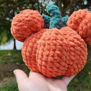 May include: A crocheted pumpkin with a green stem and orange body. The pumpkin is shaped like a Mickey Mouse head.