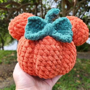 May include: A crocheted pumpkin with a green bow, resembling a popular cartoon character. The pumpkin is orange and the bow is a dark green.