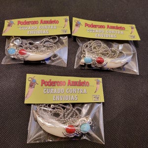 May include: Three necklaces with a silver-colored pendant shaped like a tooth, adorned with red and blue stones. Each necklace is packaged with a yellow card that has Spanish text.