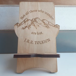 May include: Wooden phone stand with a mountain range design and the quote "Not all those who wander are lost." by J.R.R. Tolkien.