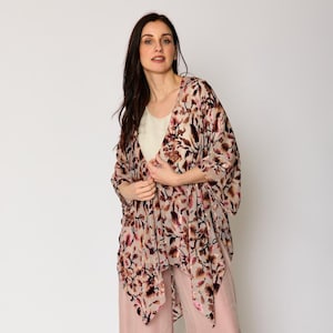 Pode incluir: Uma mulher vestindo um quimono de estampa floral rosa com um design longo e fluido. O quimono é feito de um tecido macio e sedoso e tem um caimento relaxado. A mulher também está vestindo uma calça de perna larga rosa claro.