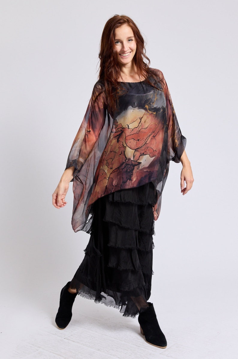 May include: A woman wearing a black and brown patterned silk top with a black tiered skirt and black ankle boots.