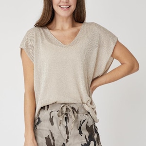 Pode incluir: Uma blusa de malha bege com decote em V e mangas curtas. A blusa é combinada com calças de estampa camuflada.
