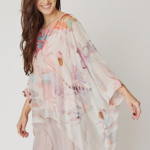Puede incluir: Una blusa fluida con estampado floral en suaves colores pastel, incluyendo rosa, melocotón y azul. La blusa tiene una silueta suelta y drapeada y se combina con pantalones rosa claro a juego. El estilo general es femenino y ligero.