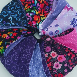 May include: A collection of fabric face masks in various patterns, including floral, paisley, and polka dots. The masks are made from a variety of fabrics, including cotton and linen. The masks are all in shades of purple, pink, and black.